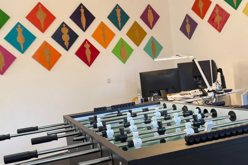 Kickertisch und Arbeitsplatz in unserem Büro, an der Wand bunte Rauten mit Figuren